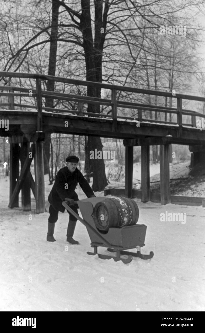 Ein Mann ein transportiert Fass Pilsener Schultheiss Schlitten auf einem durch den winterlichen Spreewald, Deutschland 1930 er Jahre. Un homme transportant un baril de bière Schultheiss sur un traîneau à travers une forêt d'hiver dans la région de Spreewald, Allemagne 1930. Banque D'Images