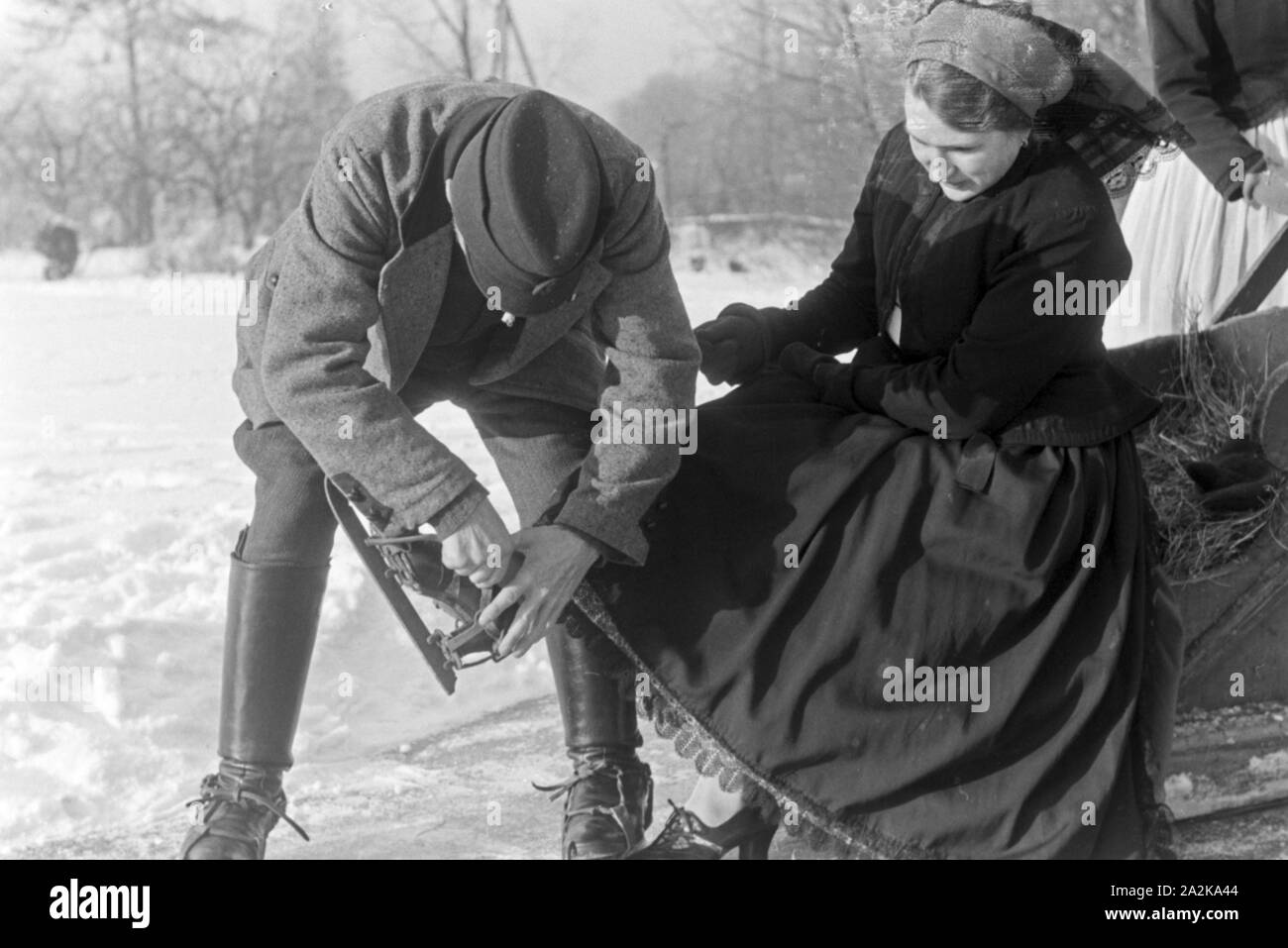 Ein Mann und Frau hilft beim Anschnallen von Schlittschuhkufen im Spreewald, Deutschland 1930 er Jahre. Un homme aide une femme à mettre sur la glace skate coureurs au Spreewald, Allemagne 1930. Banque D'Images