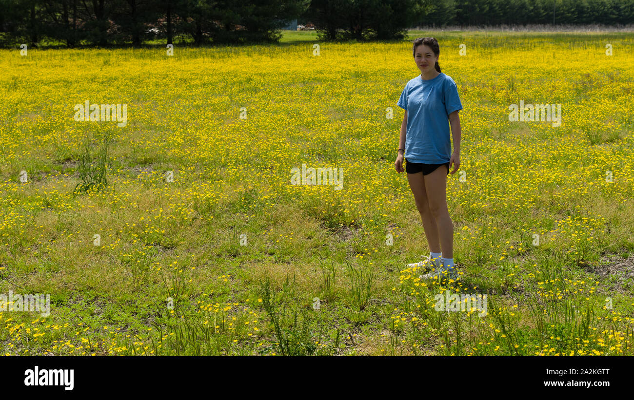 Teen girl in shorts debout dans un grand champ avec des fleurs jaunes et des arbres en arrière-plan Banque D'Images