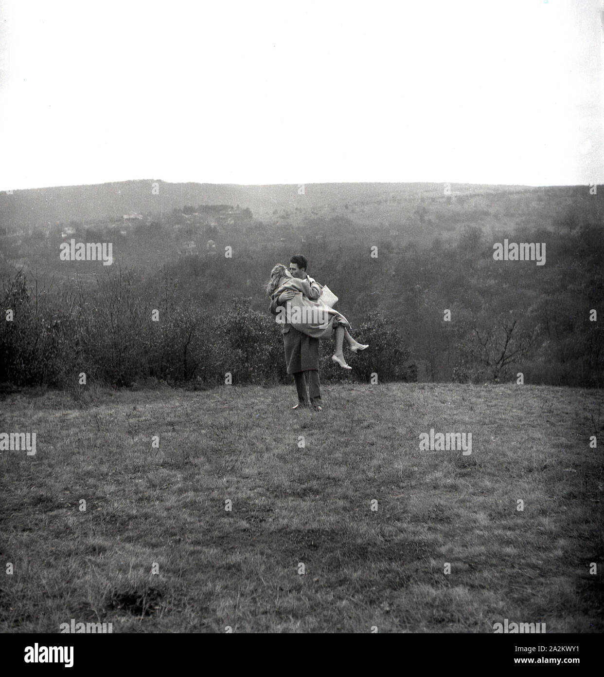 Années 1960, historique, deux amoureux sur une colline, un homme portant et embrassant sa petite amie sur une haute montagne herbeuse, Angleterre, Royaume-Uni. Banque D'Images