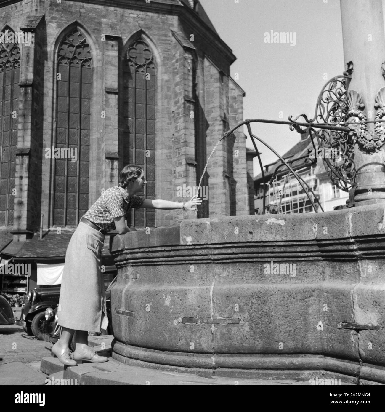 Junge Frau am Brunnen Hinter der Heiliggeistkirche à Heidelberg, Allemagne Allemagne Années 1930 er Jahre. Jeune femme d'une fontaine derrière l'église Heiliggeistkirche à Heidelberg, Allemagne 1930. Banque D'Images