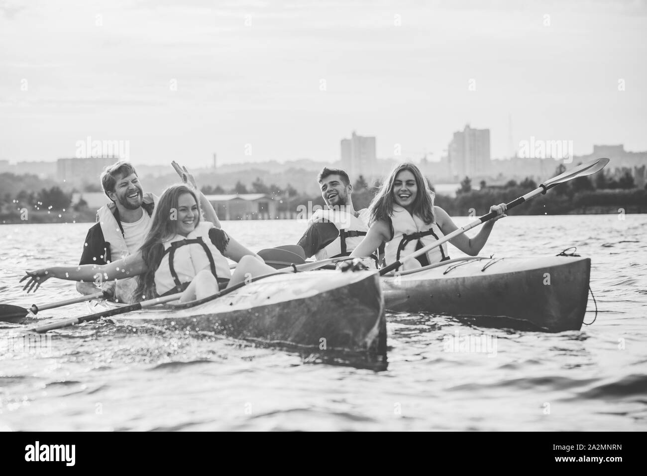 Happy young caucasian groupe d'amis du kayak sur la rivière au coucher du soleil dans l'arrière-plan. Avoir du plaisir dans l'activité de loisirs. Heureux les hommes et les femmes sur le modèle laughting kayak. Le sport, les relations concept. Banque D'Images