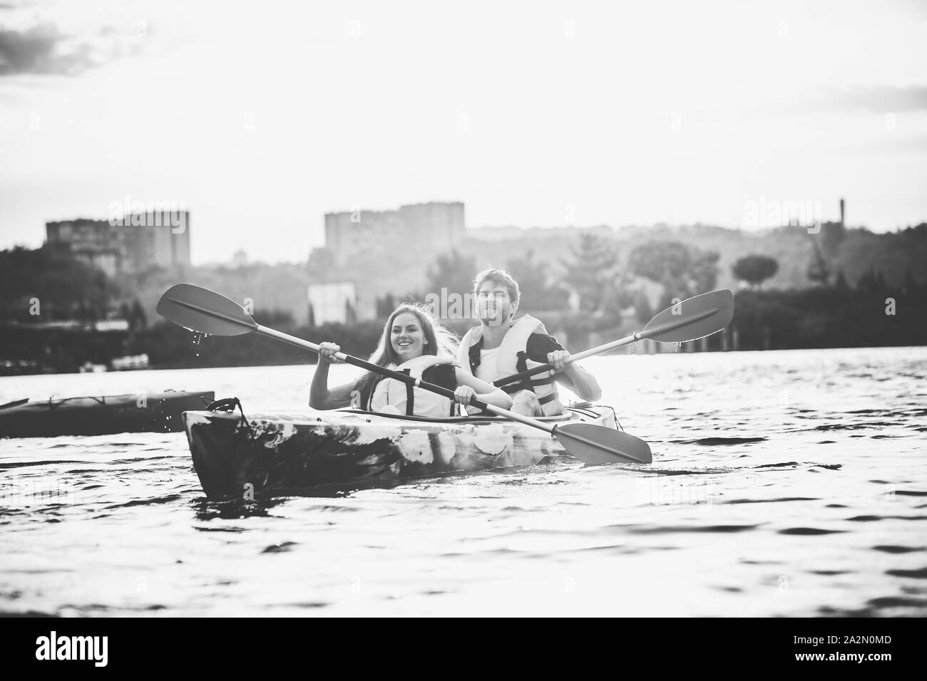 Happy young caucasian couple du kayak sur la rivière au coucher du soleil dans l'arrière-plan. Avoir du plaisir dans l'activité de loisirs. Heureux les hommes et les femmes sur le modèle laughting kayak. Le sport, les relations concept. Incolore. Banque D'Images