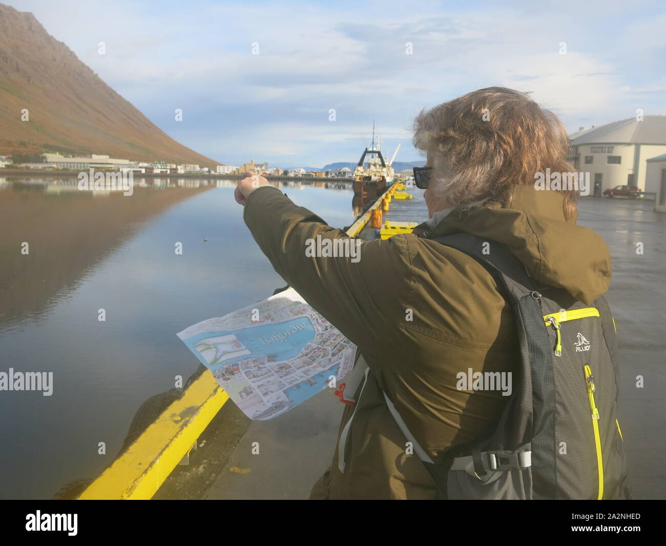 Une femme est titulaire d'une carte touristique et les points de l'autre côté de la baie sur une belle journée ensoleillée d'automne, Isajfjordur ; Westfjords, Islande Banque D'Images