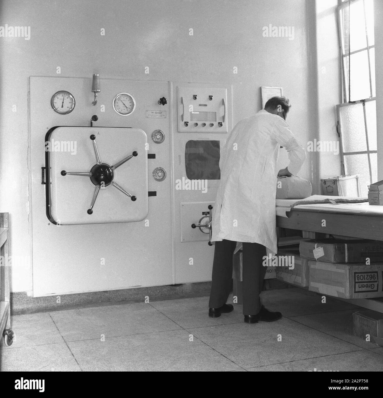Années 1960, historique, un opérateur à revêtement blanc travaillant dans une buanderie, avec une grande machine à laver industrielle « Hi Speed » montée au mur, Angleterre, Royaume-Uni. Banque D'Images