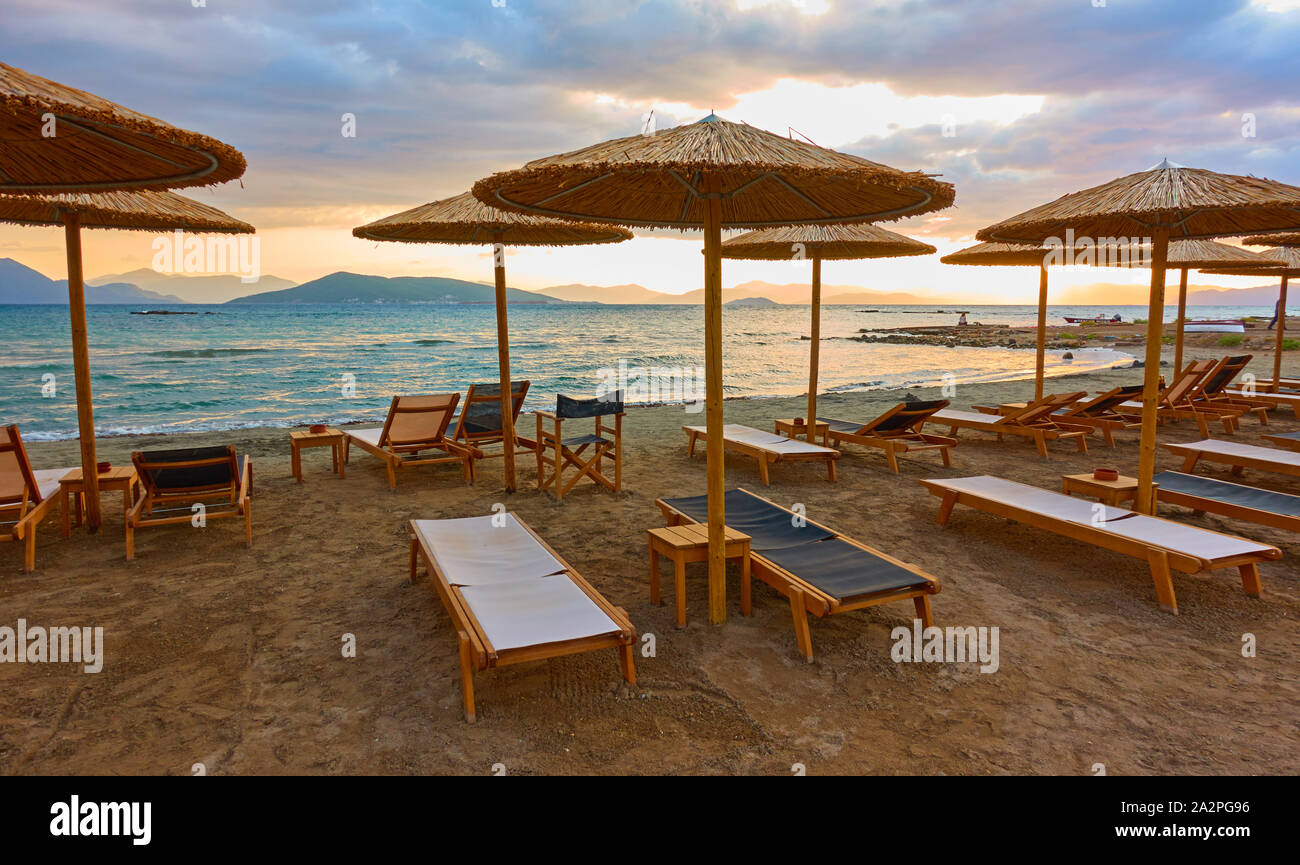 Plage avec chaises-longues et parasols de paille par la mer au coucher du soleil, l'île d'Egine, en Grèce. Vue panoramique grand angle Banque D'Images