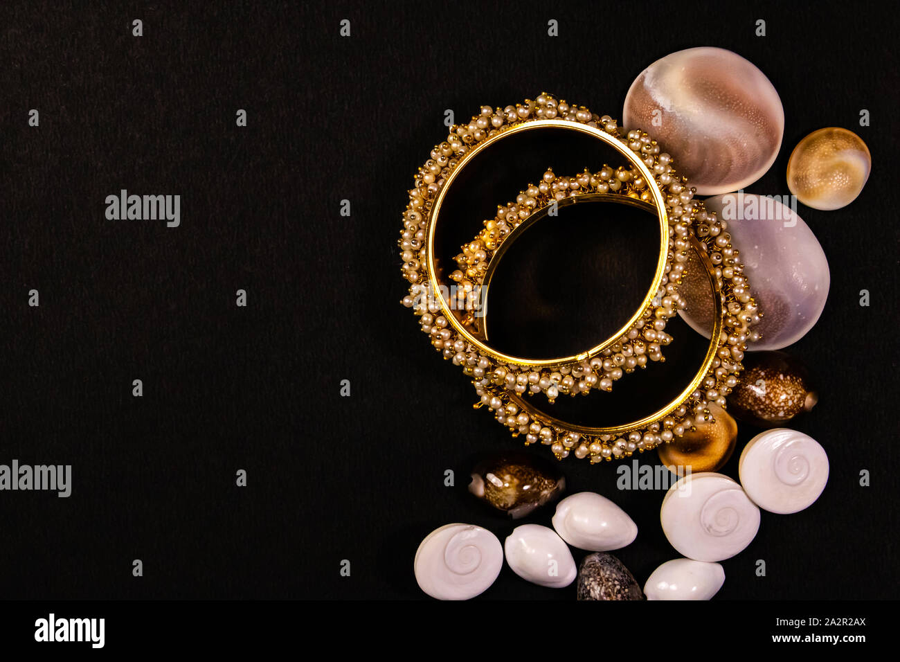 Concept de bijoux traditionnels. Belle perle plaqué or avec bangles de coquillages sur fond noir Banque D'Images