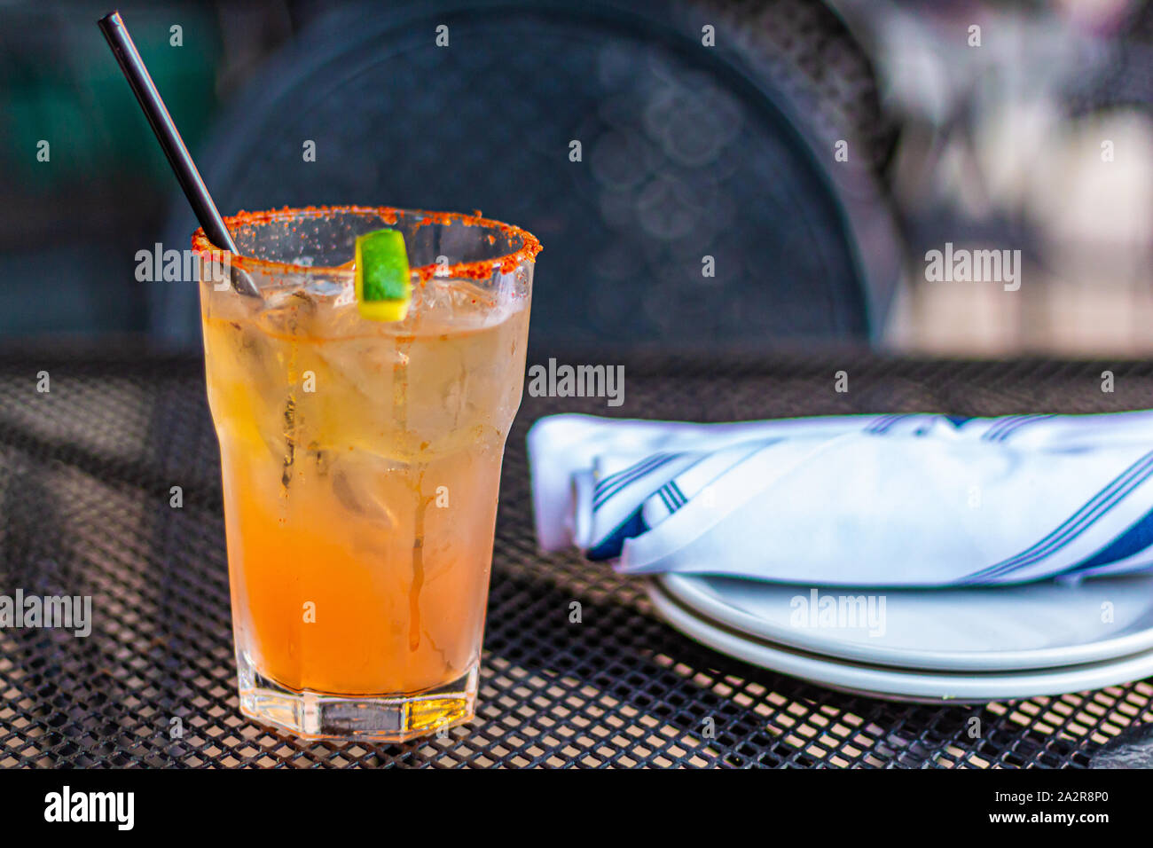 Un cocktail de couleur orange est assis sur une table en métal à côté de quelques verres et couverts, roulée dans de serviettes en tissu. Banque D'Images