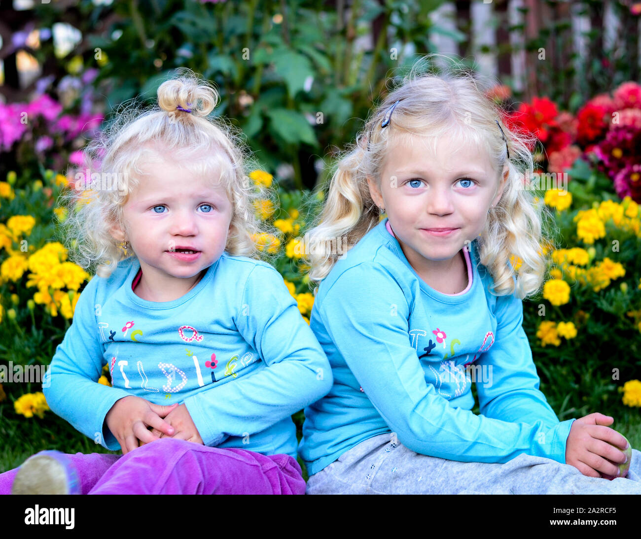 Deux beaux enfants blonds assis dans le jardin plein de fleurs colorées Banque D'Images