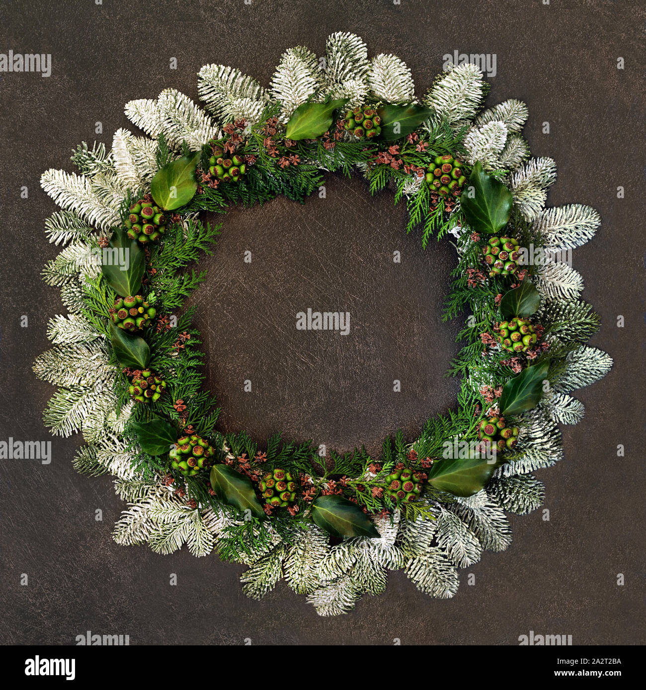 Hiver naturel et couronne de Noël avec des sapins couverts de neige, de lierre, de feuilles de cèdre et gurnge sur fond marron. Banque D'Images Hiver naturel et couronne de Noël avec des sapins couverts de neige, de lierre, de feuilles de cèdre et gurnge sur fond marron. Banque D'Images