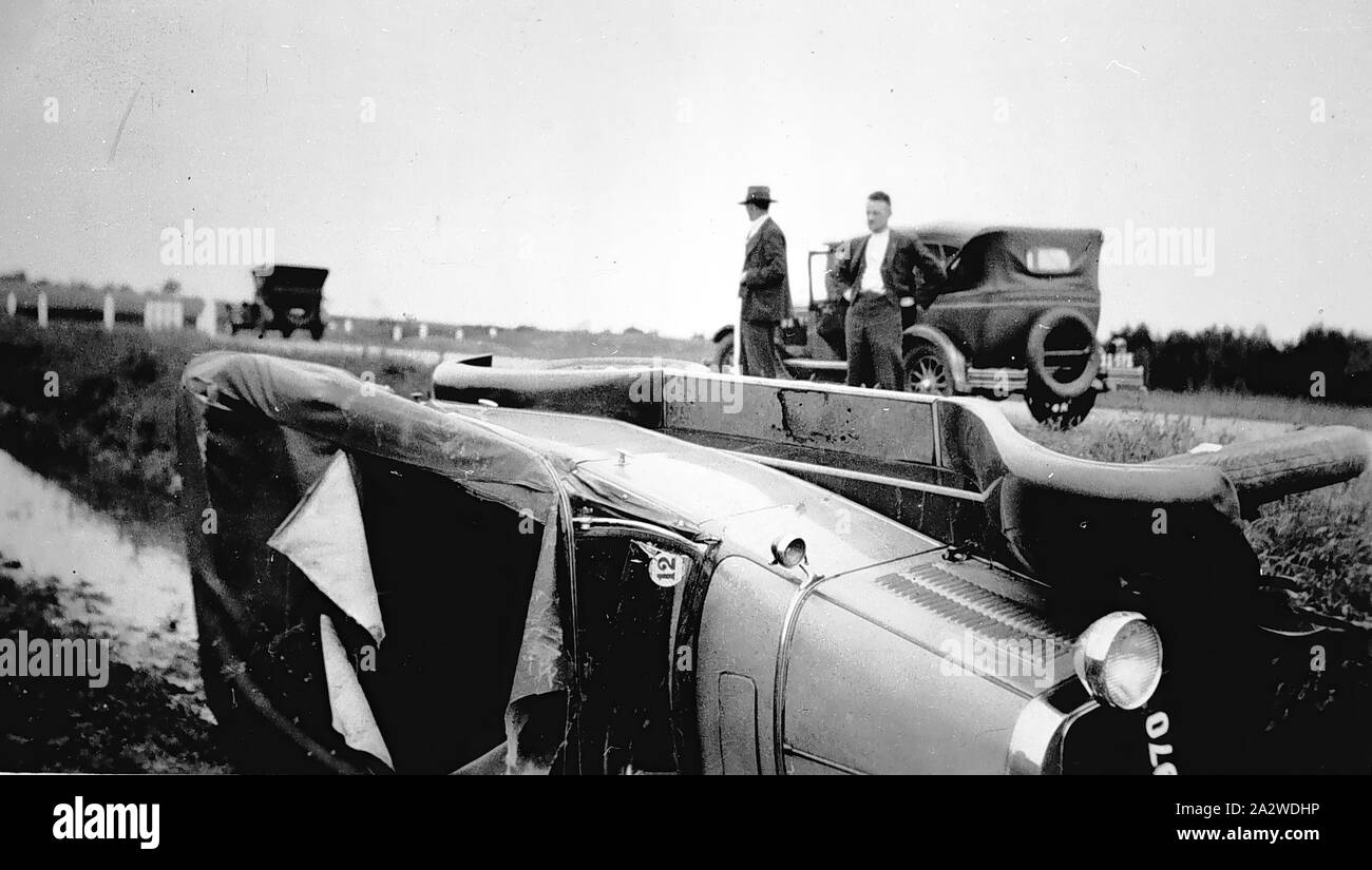 Négatif - Narre Warren, Victoria, 1934, une voiture renversée dans un fossé. Deux hommes debout à côté d'une seconde voiture sur la route, une troisième voiture est dans la distance Banque D'Images