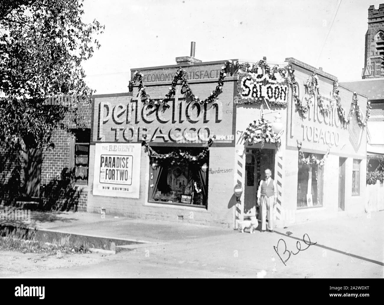 Négatif - Ballarat, Victoria, en 1938, un bureau de tabac shop & barber's saloon décorée pour l'affaire Ballarat, fêtes du centenaire. L'église Saint Pierre est en arrière-plan. Il y a une affiche d'un film publicitaire,'Paradis pour deux', sur le côté de la boutique Banque D'Images