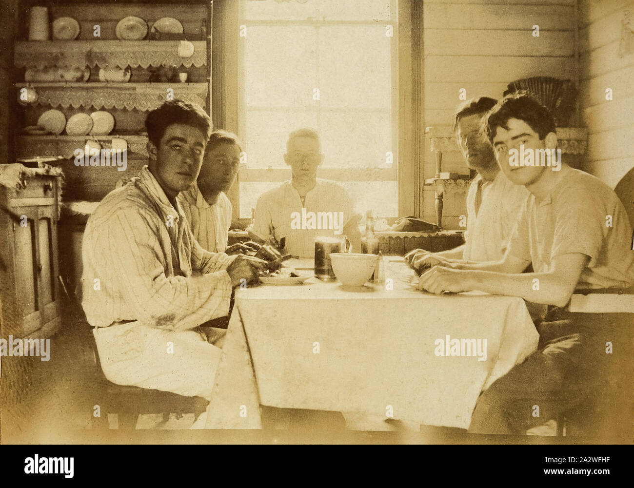 Photographie numérique - Cinq hommes manger à la table de cuisine, Chelsea, 1918, cinq jeunes hommes assis avec des couteaux et des fourchettes dans les mains autour d'une table de cuisine. Ils portent des chemises à pas de liens ou de gilets. Il y a une fenêtre juste derrière l'homme à la tête de la table. Cette photo montre Walter Burke comme un jeune homme, à l'écart sur un week-end avec un groupe d'amis appelé "Bunyips" à Chelsea, Décembre 1918 Banque D'Images