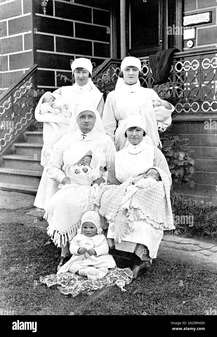 Négatif - Victoria, 1924, quatre infirmières détenant des bébés. Il y a un bambin assis sur le sol devant Banque D'Images