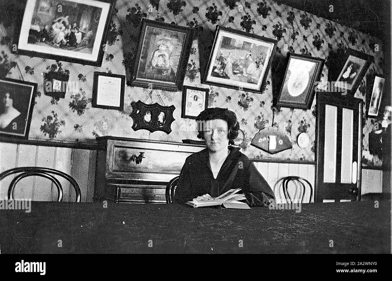 - Négatif Inverloch, Victoria, 1930, une femme à l'intérieur d'un magasin de thé. Elle est assise à une table et a un livre devant elle. Il y a un piano derrière elle et beaucoup d'images sur le mur Banque D'Images