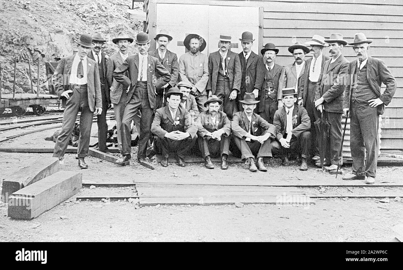 Négatif - Mount Morgan, Queensland, 1915, un groupe d'hommes à l'extérieur d'un bâtiment de la mine Mt Morgan. Ils sont tous habillés en costumes et portent des chapeaux et cravates Banque D'Images