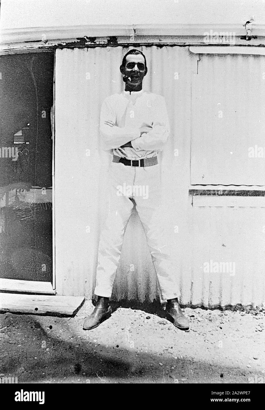 - Négatif Isisford, District de Queensland, vers 1910, un jackaroo sur 'Portland Downs' station. Il pose, les bras croisés et fumant une pipe, en face d'un hangar Banque D'Images