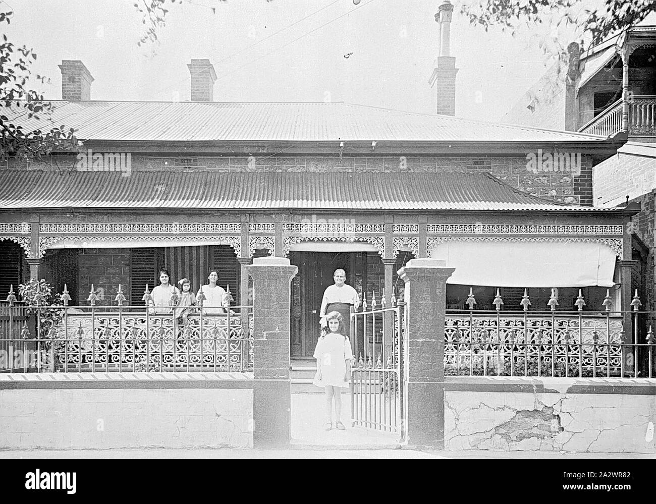 Négatif - à l'ouest de Torrens, Adélaïde, Australie du Sud, 1921, un groupe de femmes et d'enfants devant une maison. Un enfant se tient à la porte tandis que les autres se tiennent sur la véranda. La maison dispose d'auvents en toile sur la véranda Banque D'Images