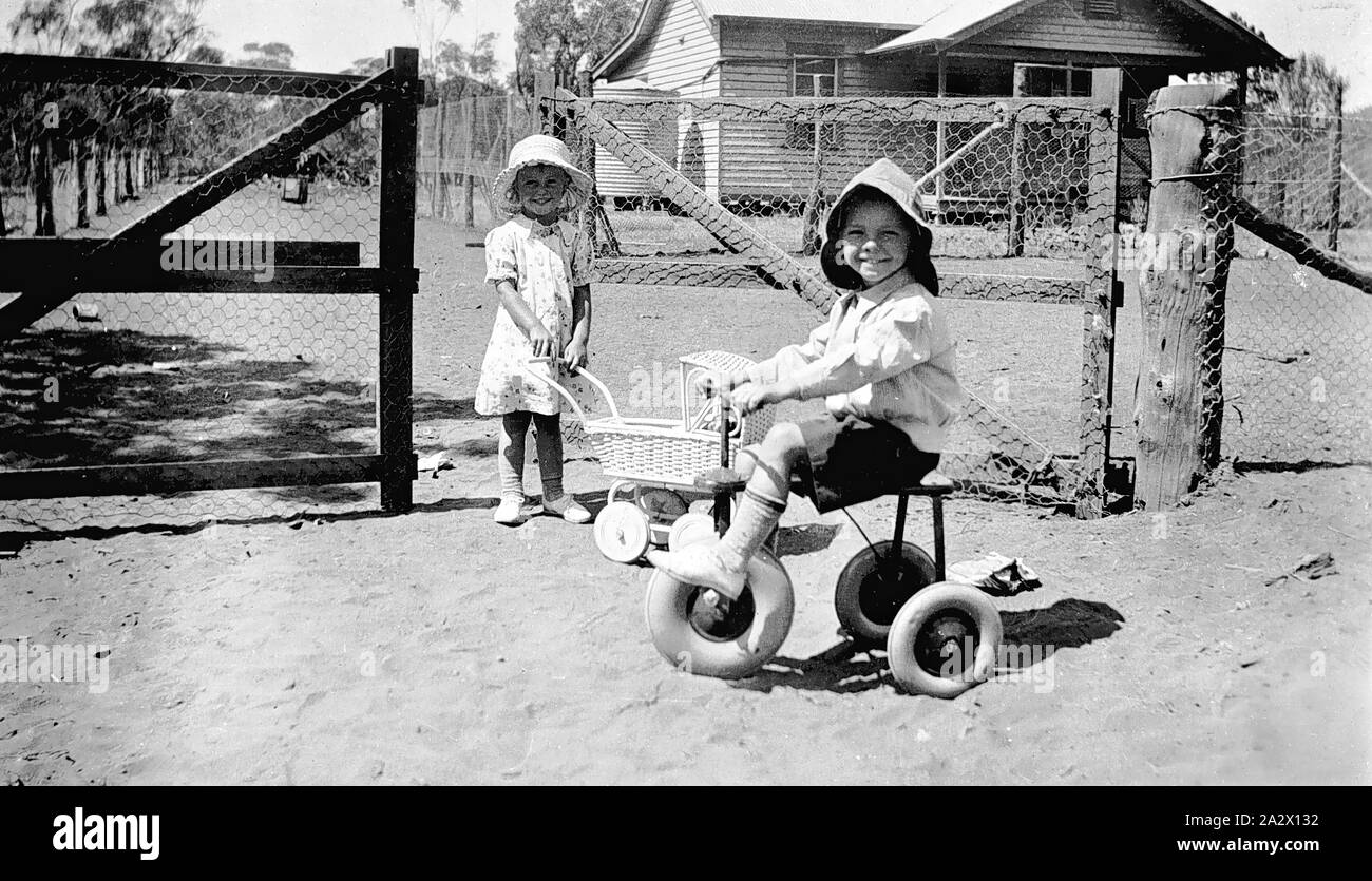 Négatif - Enfants jouant, Werrimull Sud, Victoria, 1935, les enfants qui jouent, avec garçon et fille jouet tricycle avec pram Banque D'Images