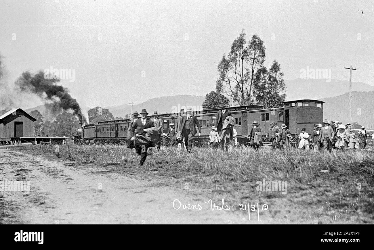 - 'Négatif', Vale Fours Myrtleford, Victoria, 21 mars 1919, Hommes, femmes et enfants de marcher à travers l'herbe haute de la gare qu'ils viennent de quitter. Le train avait été affrété pour une liquidation à 'Happy Valley' homestead. La locomotive à vapeur a établi à côté d'un petit bâtiment en bois, qui est peut-être un abri de marchandises Banque D'Images
