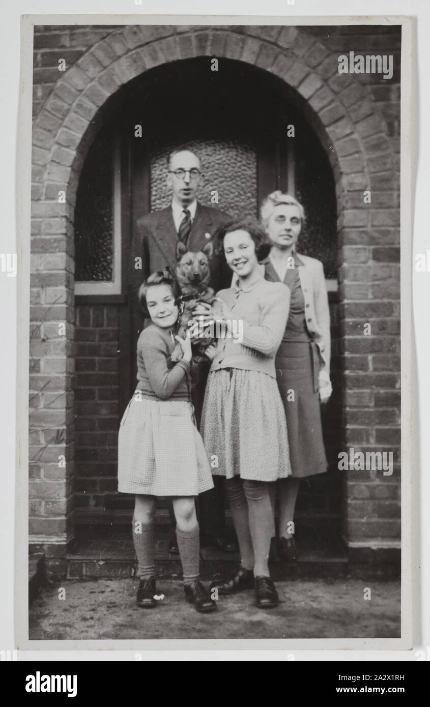 Photographie - Maison à l'extérieur de la famille Palmer, Iver, en Angleterre, vers 1947, photographie noir et blanc de George et de Gertrude Palmer et leurs filles Shirley et Lesley, et de leur chien Robbie, en Angleterre autour de 1947. Il a probablement été prise à la George's Sister's house en Iver, Buckinghamshire par George's beau-frère David Roberts, la veille de leur départ pour l'Australie. Il a été porté à l'Australie par George Palmer lorsqu'il a émigré en Australie depuis l'Angleterre avec sa femme Banque D'Images