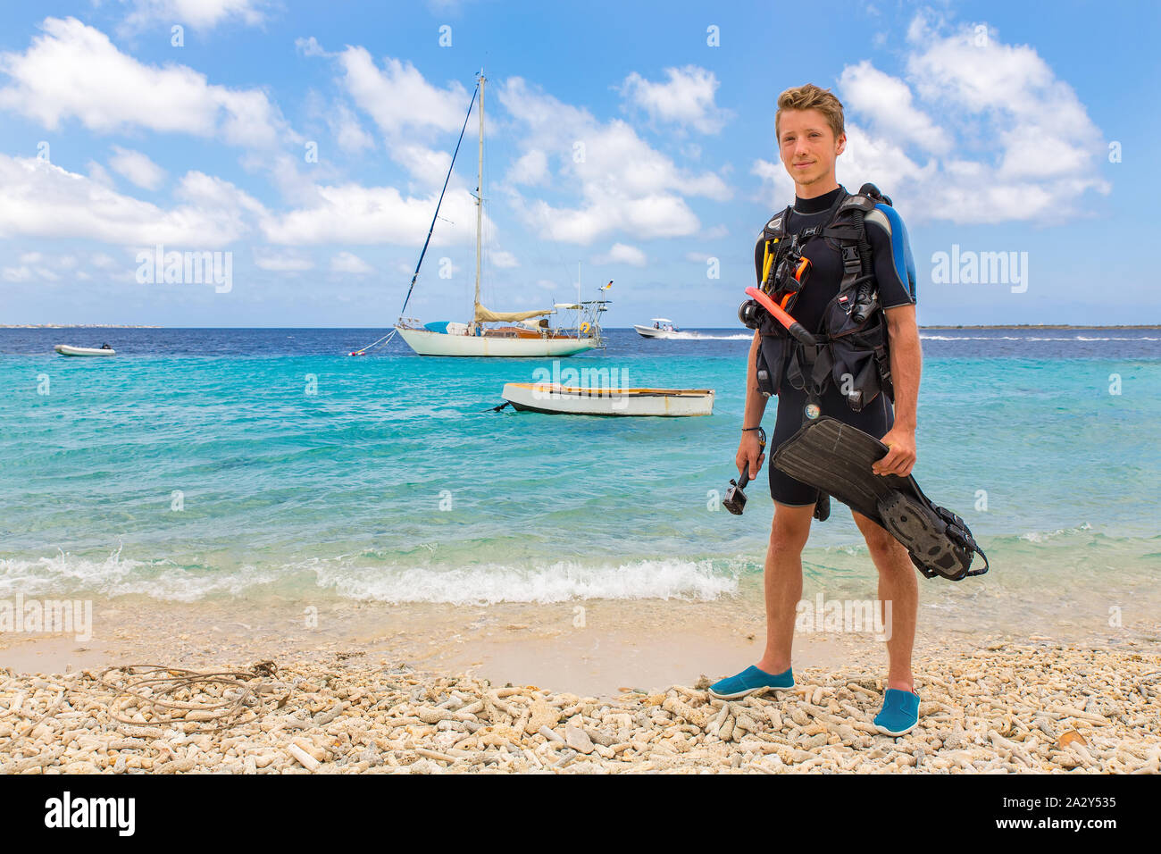 Homme de race blanche diver se dresse sur plage de Bonaire avec vue mer et bateaux Banque D'Images