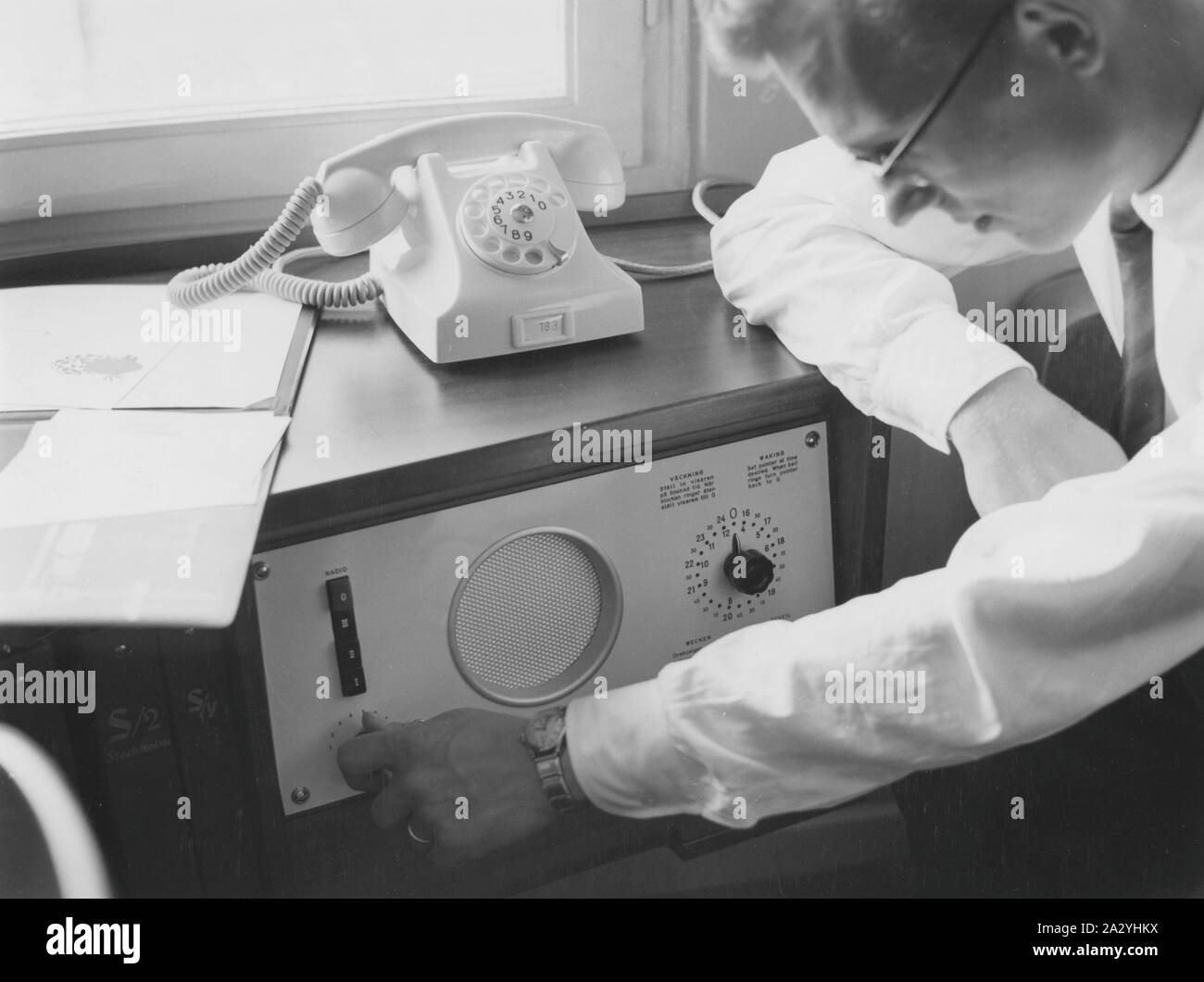 Un client de l'hôtel est à l'aide de la chambre d'hôtel radio et change de chaîne. À droite sur l'écran, il peut saisir le moment où il veut l'alarme se déclenche sur son réveil. 1957 Banque D'Images