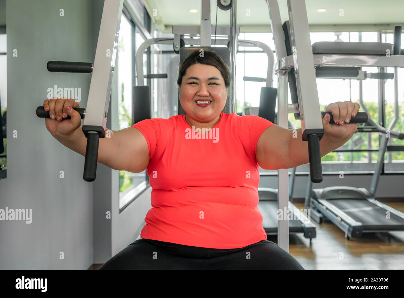 Surpoids asiatique femme jouant de l'équipement de sport pour l'exercice de bâtir sa boday seul dans une salle de sport, plaisir et sourire pendant l'entraînement. Grosses femmes prendre soin de la santé Banque D'Images