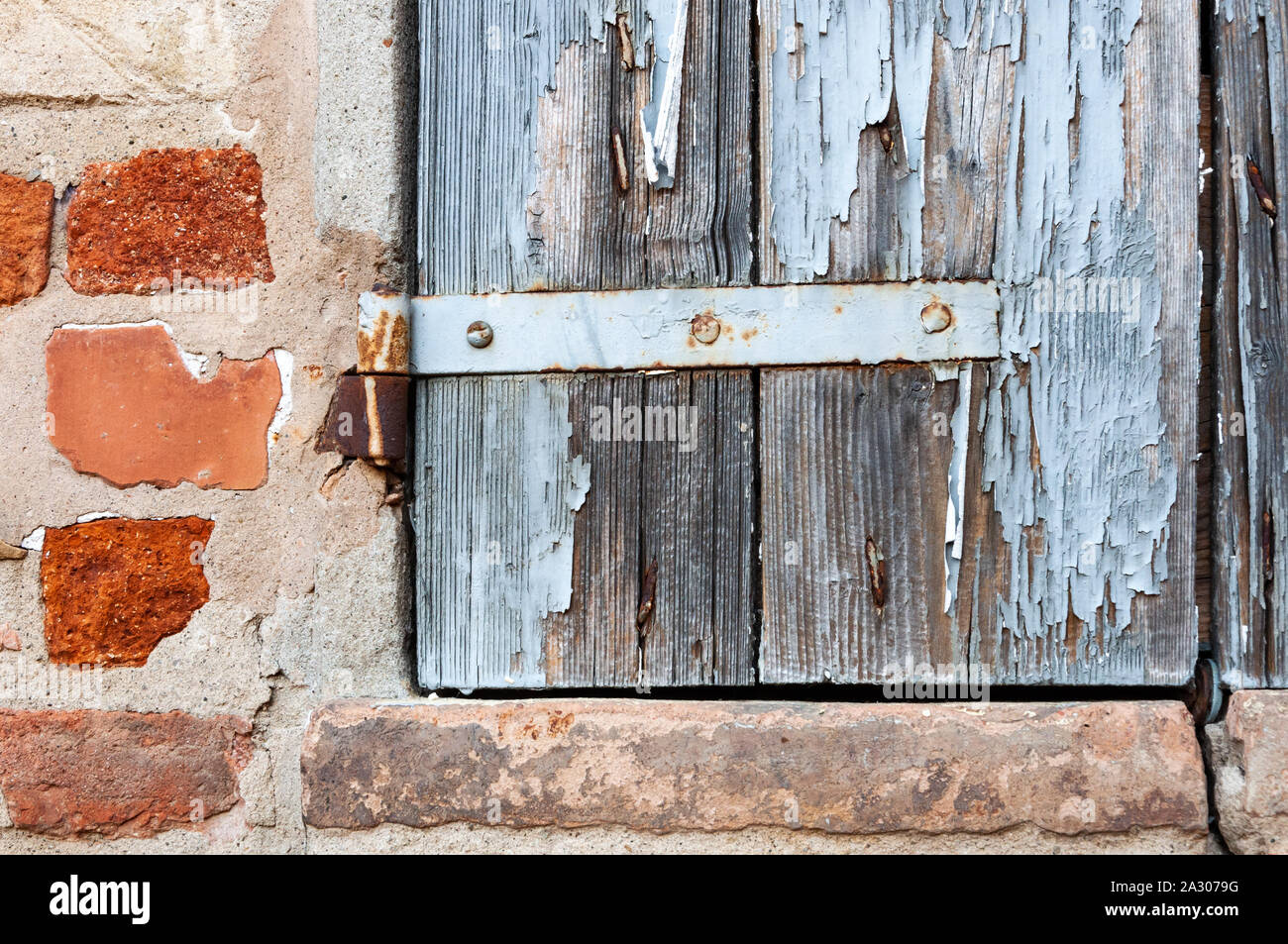 Détail de la fenêtre de maison rurale, avec peinture craquelée et charnières rouillées, sur mur de briques et de pierres anciennes. Banque D'Images