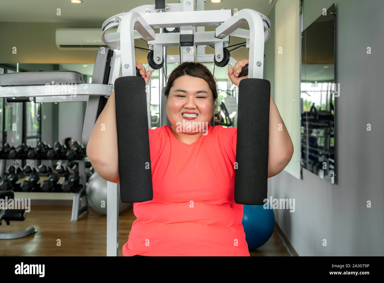 Surpoids asiatique femme jouant de l'équipement de sport pour l'exercice de bâtir sa boday seul dans une salle de sport, plaisir et sourire pendant l'entraînement. Grosses femmes prendre soin de la santé Banque D'Images
