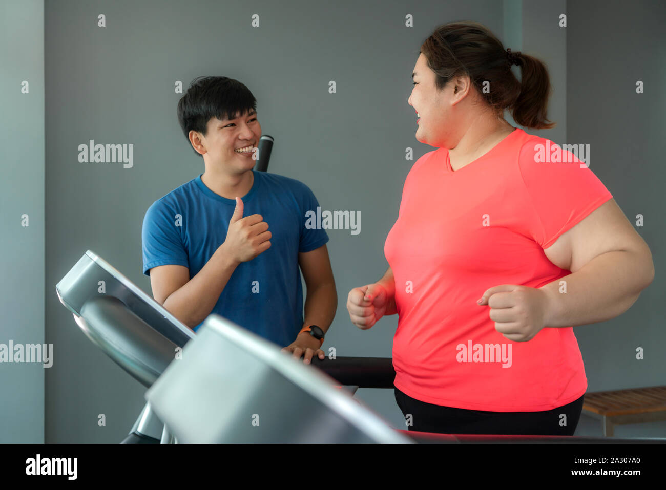 Deux formateurs de l'Asie et de l'embonpoint homme femme l'exercice de formation sur tapis roulant dans une salle de sport, formateur thump vers elle pour bon résultat lors de l'entraînement. Grosses Femmes Banque D'Images