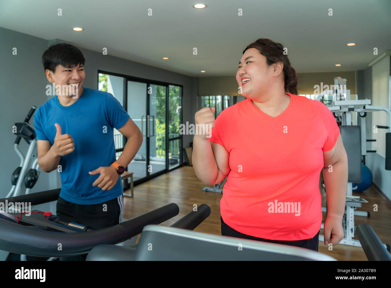 Deux formateurs de l'Asie et de l'embonpoint homme femme l'exercice de formation sur tapis roulant dans une salle de sport, formateur thump vers elle pour bon résultat lors de l'entraînement. Grosses Femmes Banque D'Images