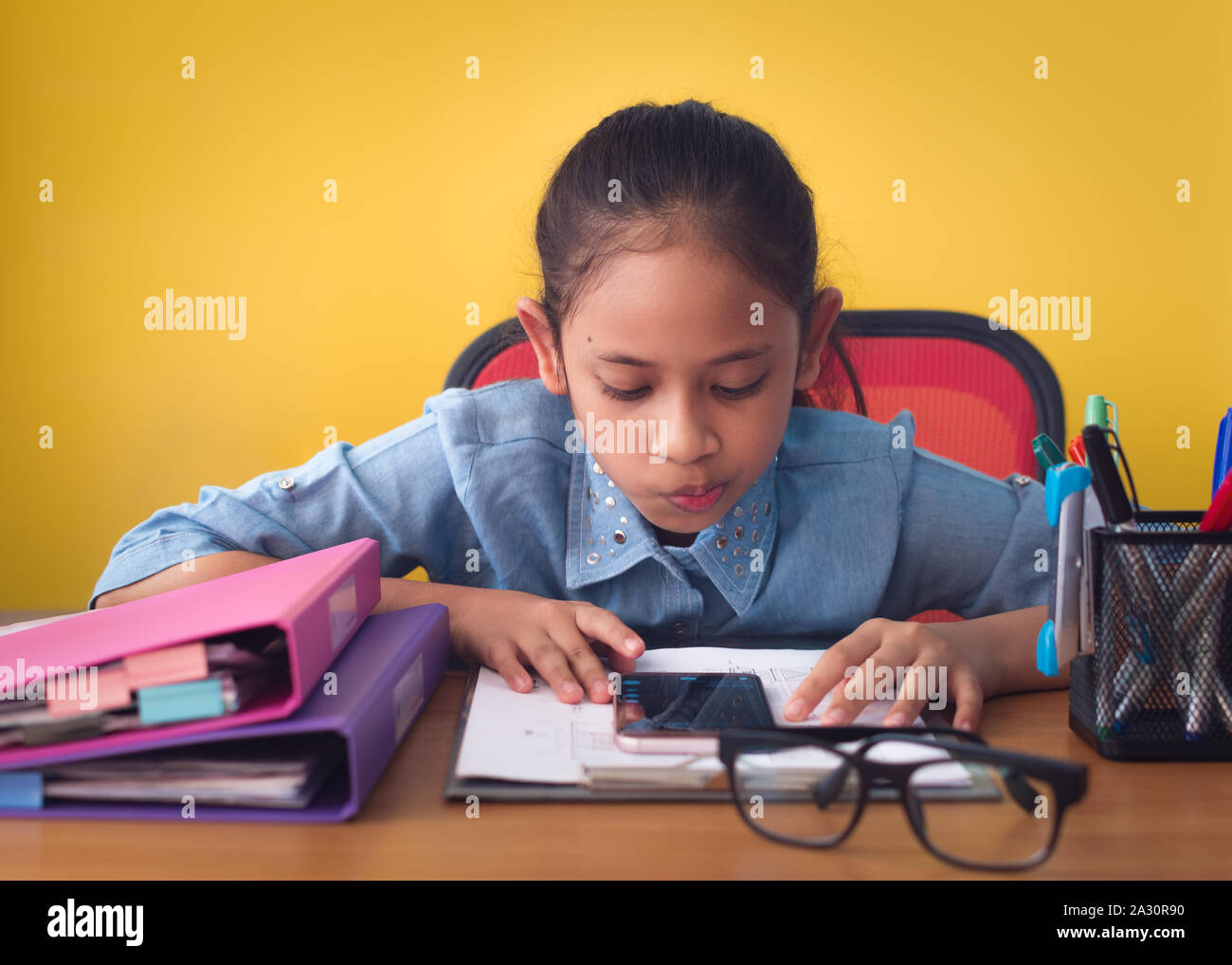 Jolie fille à l'aide de téléphone mobile sur le bureau isolé sur fond jaune. Concept de réalisation. Banque D'Images