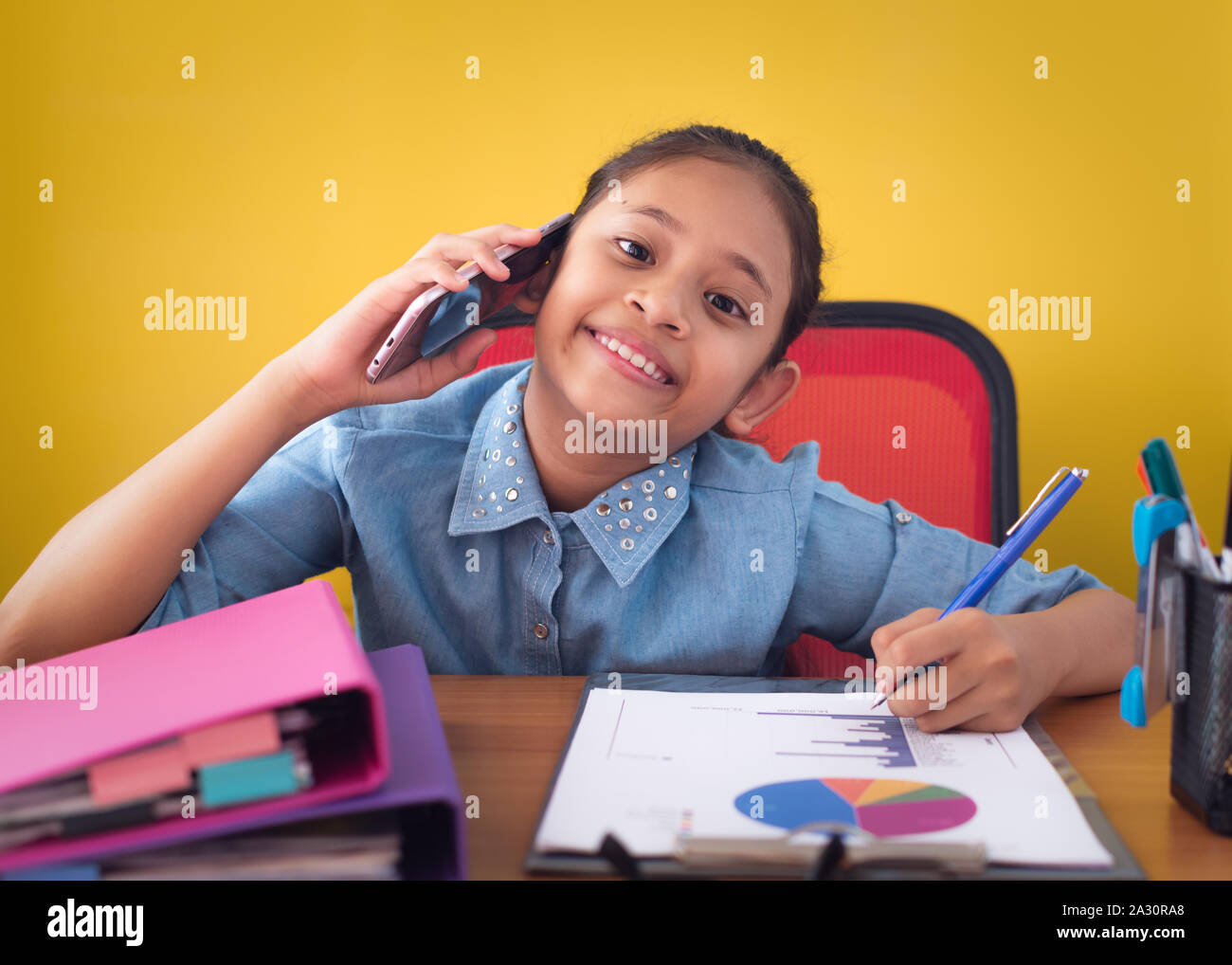 Cute girl using mobile phone et souriant sur le fond jaune isolé 24. Concept de réalisation. Banque D'Images