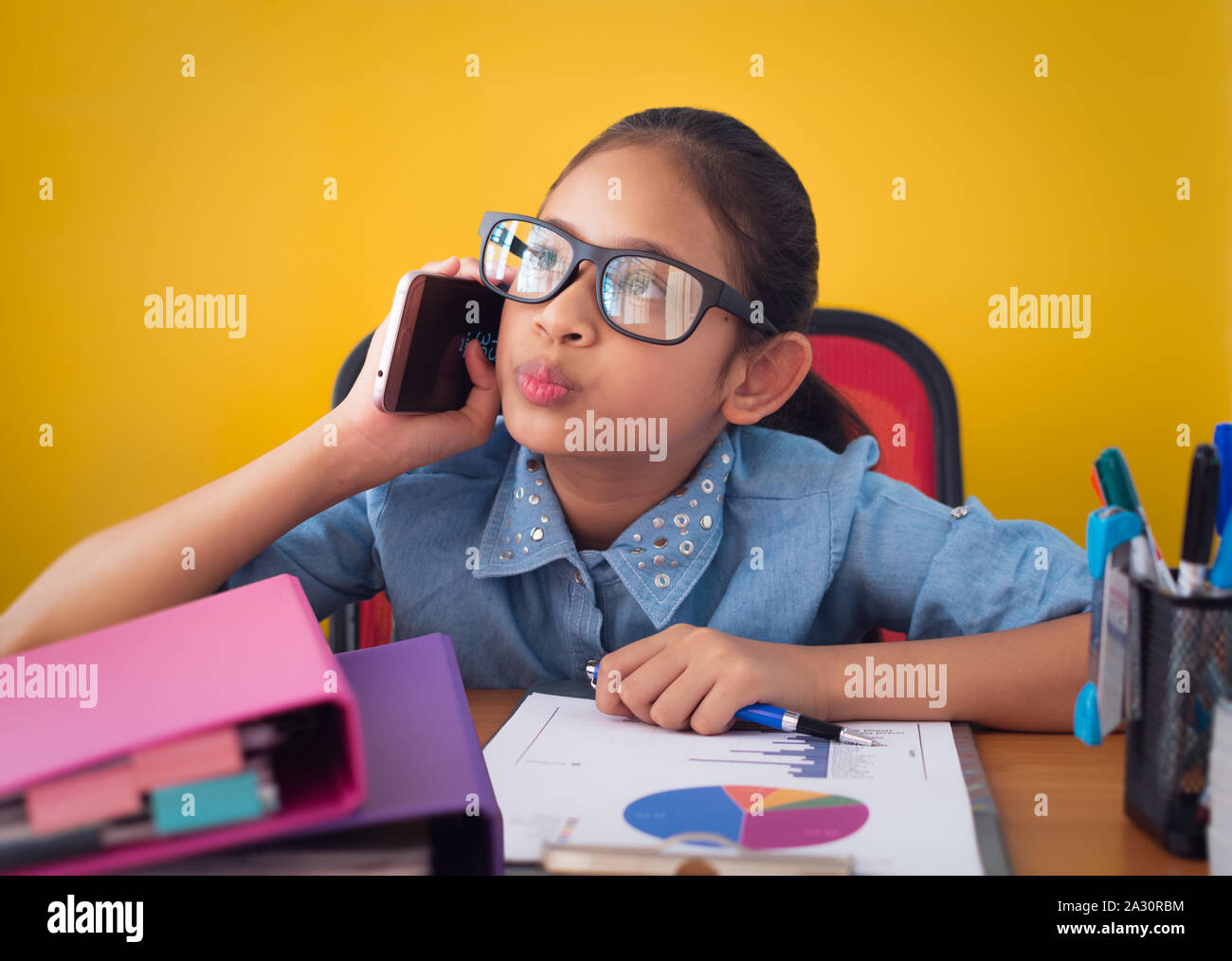 Cute girl penser et parler au téléphone au bureau isolé sur fond jaune, l'éducation et de la communication concept. Banque D'Images