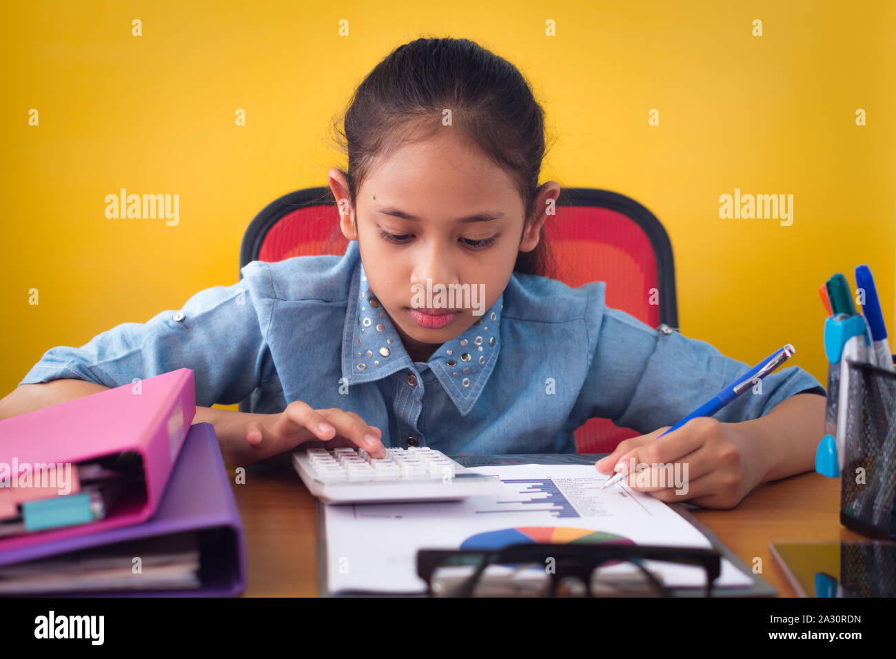 Cute girl travailler avec la calculatrice sur le bureau avec isolé document fond jaune. Concept de l'éducation. Banque D'Images