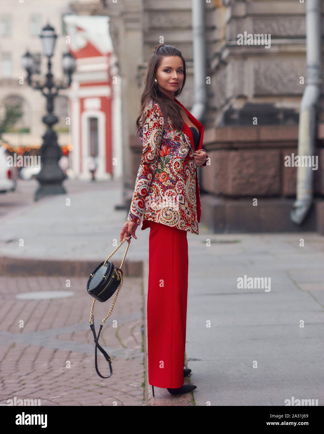 Femme en costume rouge coloré au pied de la rue de la vieille ville.  Élégant à la mode fille en manteau rouge, pantalon et sac à main en cuir  noir lunettes maintenant