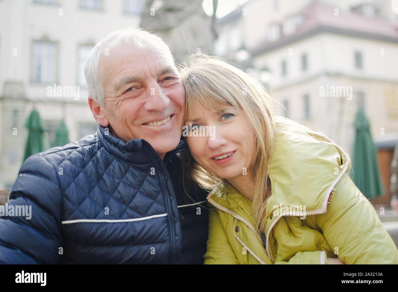 Bel homme âgé est embrassant sa jeune femme blonde de passer du temps ensemble à l'extérieur dans l'ancienne cité au début du printemps ou en automne. Banque D'Images