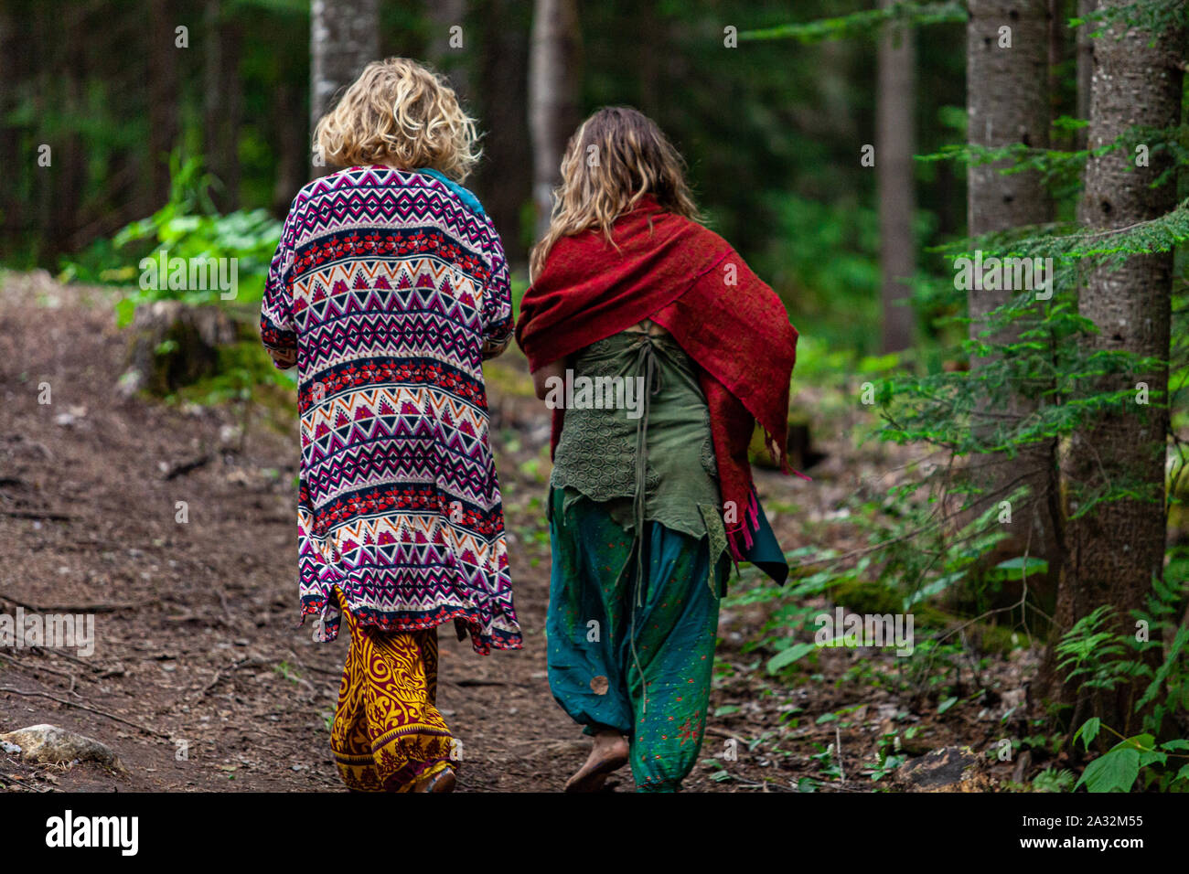 Deux femmes portant une décoration lumineuse et colorée de style bohème  vêtements sont vus de dos, marcher ensemble à travers un sentier forestier  au cours d'une retraite à l'esprit Photo Stock -