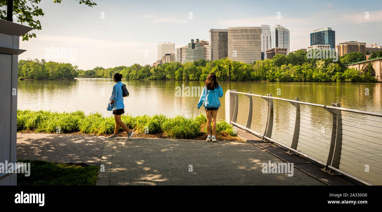 Deux femmes debout par rivière en manteaux bleu avec les immeubles de bureaux dans l'arrière-plan Banque D'Images