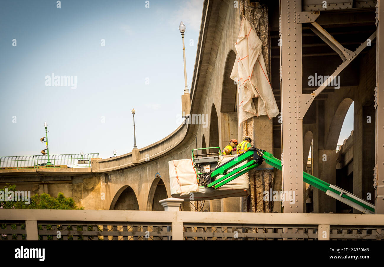 Deux travailleurs avec un casque dans un seau de travailler sur un pont Banque D'Images