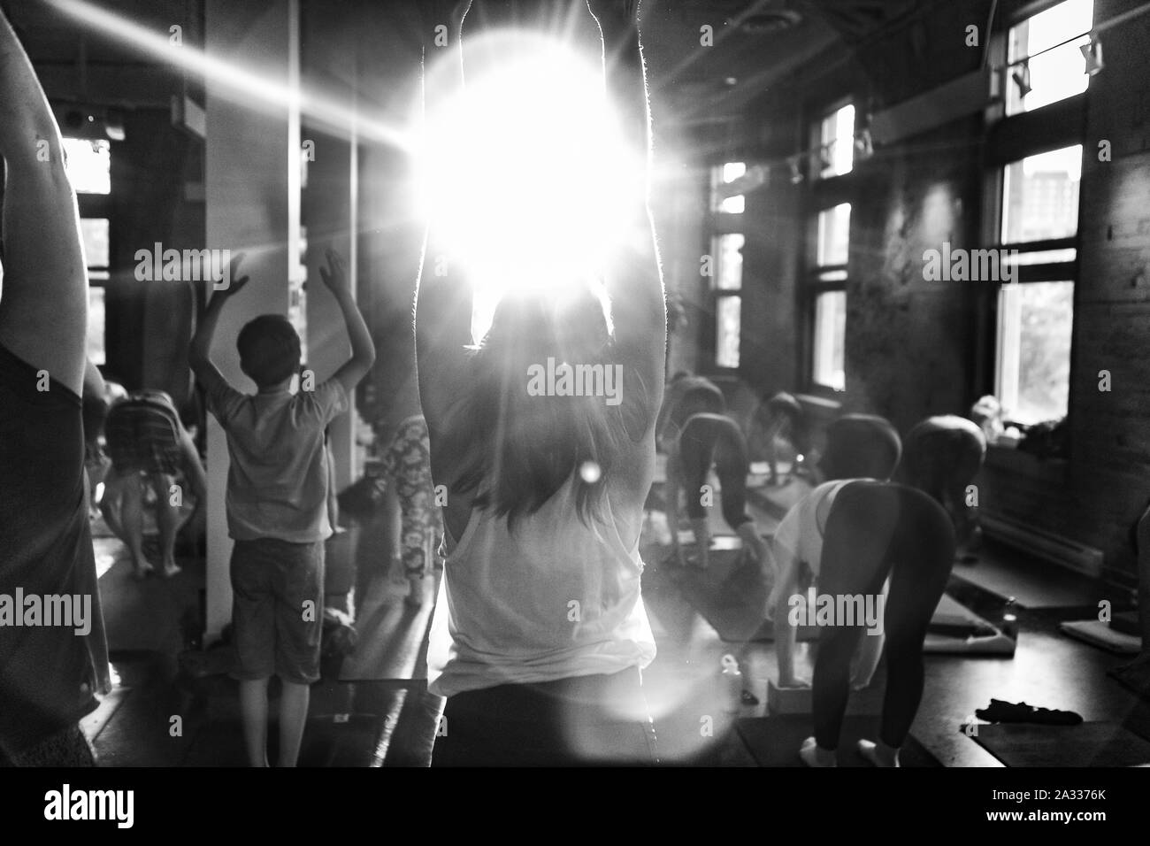 Un retour éclairé, noir et blanc vue d'une femme faisant la part à la hausse au cours de stretch 108 salutations au soleil, avec des reflets comme elle fait face à la lumière du soleil. Banque D'Images