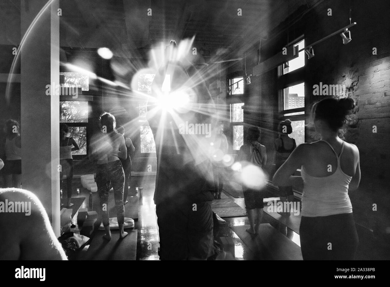 Une vue monochrome de l'arrière d'une grande salle de sport comme les participants sont vu l'adoration du soleil pendant 108 cycles de surya namaskar. Objectif lumineux éclat donne le ton. Banque D'Images