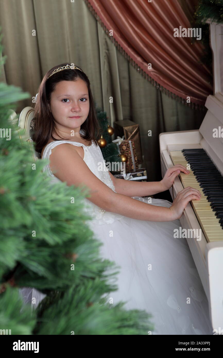 Belle jeune fille en robe blanche joue du piano Banque D'Images