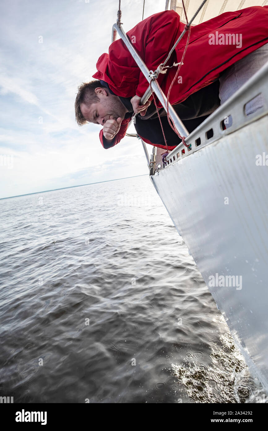 Un homme en veste rouge souffre de mal en marchant sur un yacht. Banque D'Images