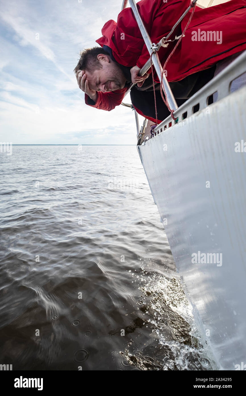 Un homme en veste rouge souffre de mal en marchant sur un yacht. Banque D'Images