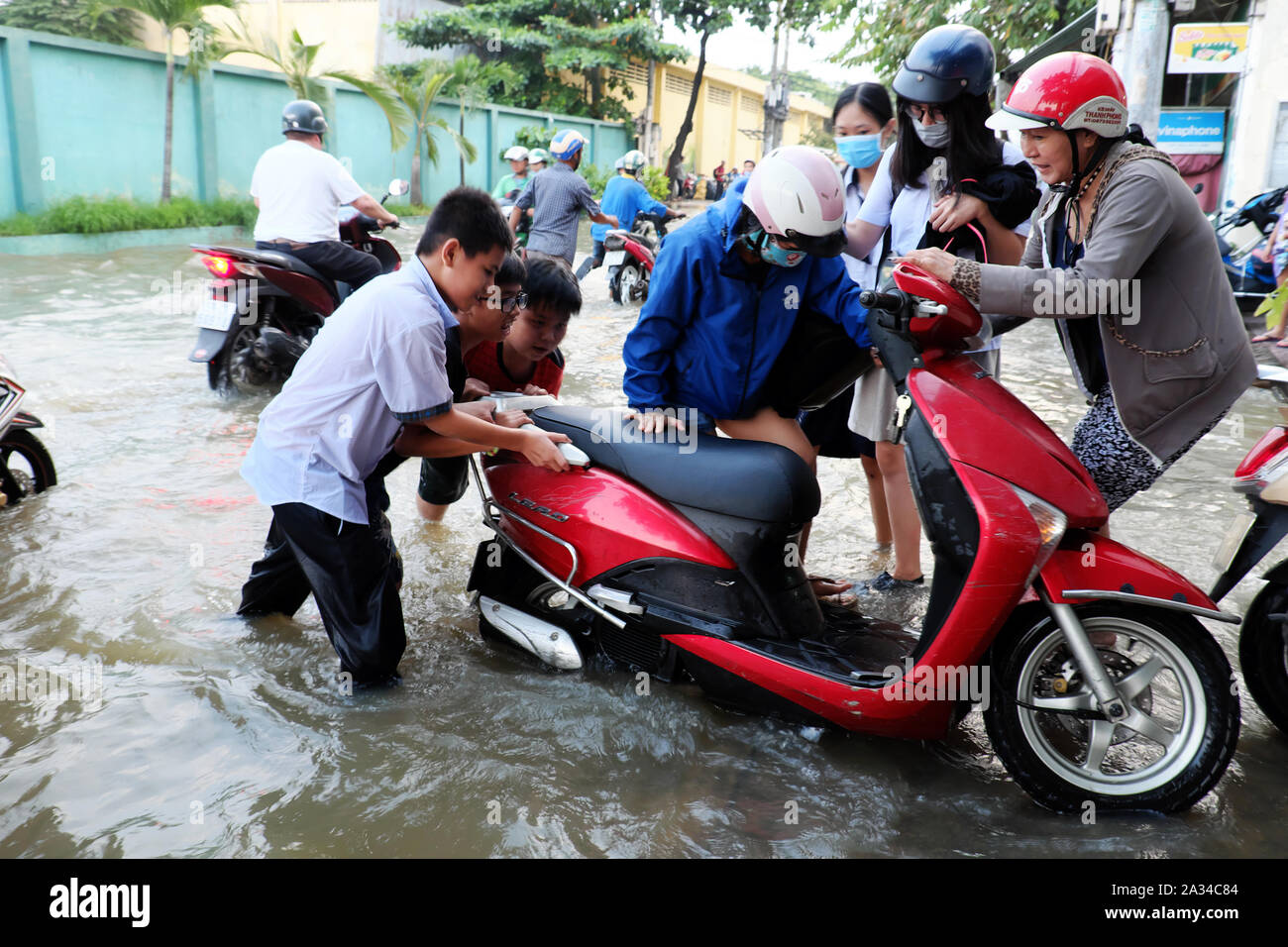 HO CHI MINH VILLE, VIET NAM, les petits garçons aident les femmes à pousser  la moto que le moteur tombe en panne dans l'eau sur la rue inondée par la  marée haute