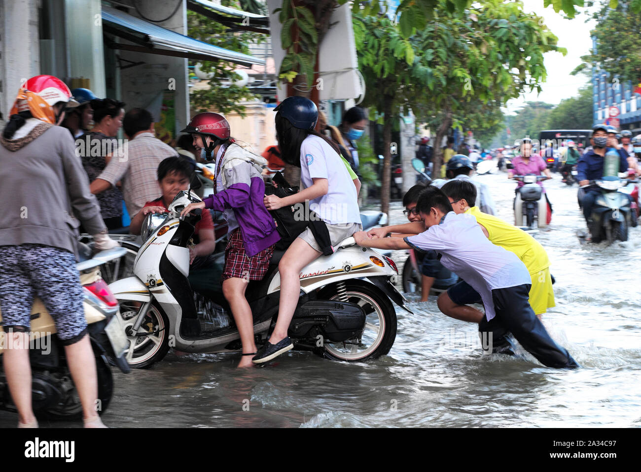 HO CHI MINH VILLE, VIET NAM, les petits garçons aident les femmes à pousser la moto que le moteur tombe en panne dans l'eau sur la rue inondée par la marée haute à la chaussée Banque D'Images