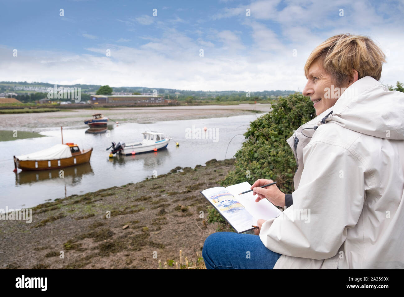 Retraite Senior woman encombrement à l'extérieur, près de l'estuaire du fleuve en vacances au Royaume-Uni, portant des vêtements chauds occasionnels Banque D'Images