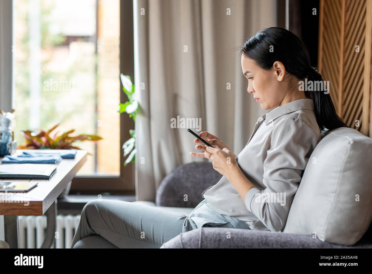 Jeune femme avec le smartphone assis sur table en restaurant et de messagerie Banque D'Images